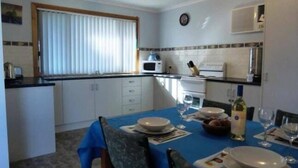 Une cuisine compacte avec des meubles blancs, un four à micro-ondes et un évier. On y trouve une table à manger, mise avec des assiettes et des verres.