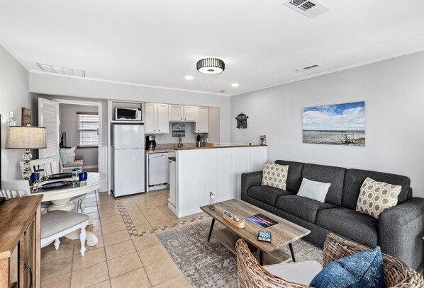 A modern kitchen with white cabinets, a central island, and a dining area with a table and chairs. - Breaking Away 1br/1ba + Sleeper, 2nd fl Ocean Peek (Isle of Palms)
