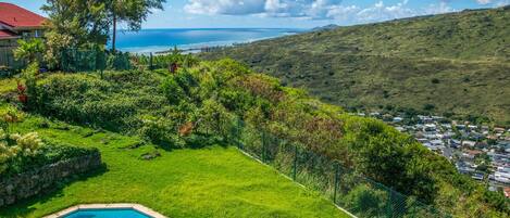 A residential property with a swimming pool, lush greenery, and a view of a coastal town.