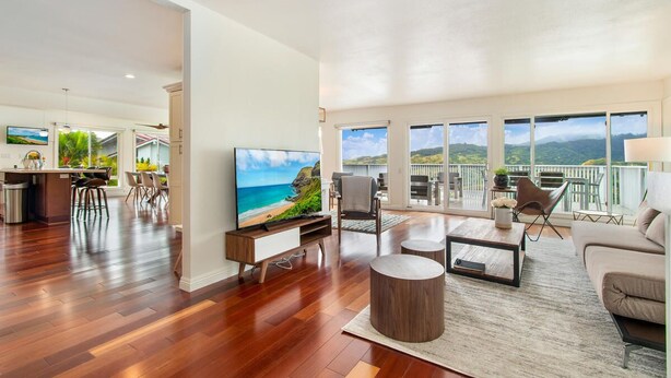 Ampla sala de estar com uma TV grande, piso de madeira e varanda com vista panorâmica.