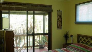 Ein Schlafzimmer mit Bett, Ventilator, Fenster und Blick ins Freie.