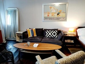 Una moderna camera d'albergo con un divano grigio scuro, cuscini decorati, un tavolino in legno e un quadro appeso al muro.