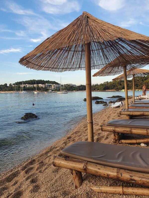 En strand med parasoller av halmtak och solstolar.