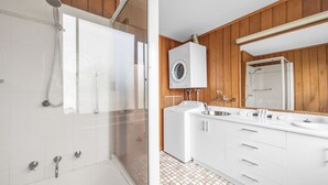 A modern bathroom with a shower, a built-in washing machine, and a vanity with a large mirror. - Coolabah Court - Merimbula (Merimbula)