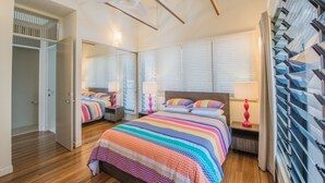 Un dormitorio con una cama grande, dos mesitas de noche, un ventilador de techo y una ventana con persianas.