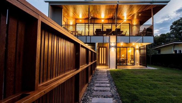 Una casa moderna de dos pisos con fachada de madera, un balcón y una entrada bien iluminada.