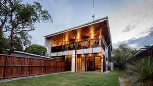 Una casa moderna de dos pisos con un balcón, un patio cubierto y un césped bien cuidado.