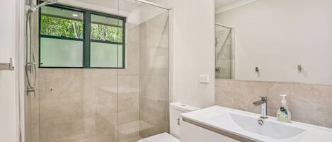 A modern bathroom with a glass shower enclosure, a toilet, and a sink with a mirror above.