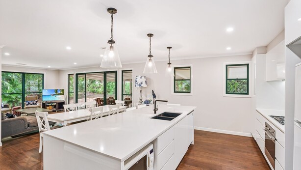 A modern kitchen with a central island, white cabinetry, and a large window overlooking greenery. - 7 Belle Court - Rainbow Shores. Huge Beach House! Pets Welcome. Property not fenced. Ducted aircon (RAINBOW BEACH)