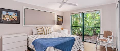 A bedroom with a bed, a nightstand, a chair, and a window with a view of greenery.