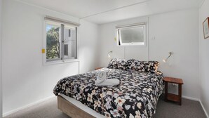 Een slaapkamer met een bed, twee ramen, een nachtkastje en een wandlamp.