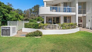Una casa moderna de varios pisos con fachada blanca, balcón con barandas de vidrio y césped cuidado.