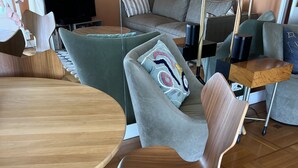 Un salon moderne avec une table à manger en bois, un canapé gris agrémenté d’un coussin coloré et une chaise en bois.