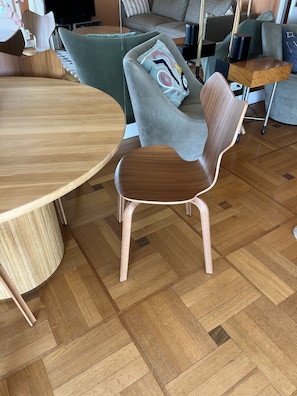 A modern living room with a wooden dining table, a grey sofa with a colorful pillow, and a wooden chair. - NICE MOST AMAZING SEA + MOUNTAIN VIEWS ,2 A/C BEDROOMS,GARAGE FOR EV,3TERRACES (Nice)