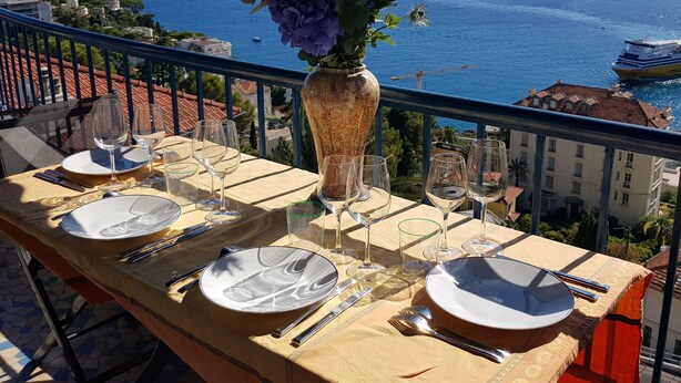 Une table dressée pour deux personnes, avec vue sur la mer et des bâtiments en arrière-plan.