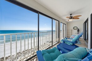 Un balcón con vista a la playa, sillones reclinables azules y un ventilador de techo.