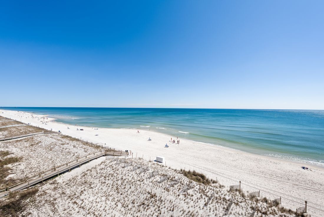A beach with a wooden boardwalk leading to the shore, sandy dunes, and clear blue water.