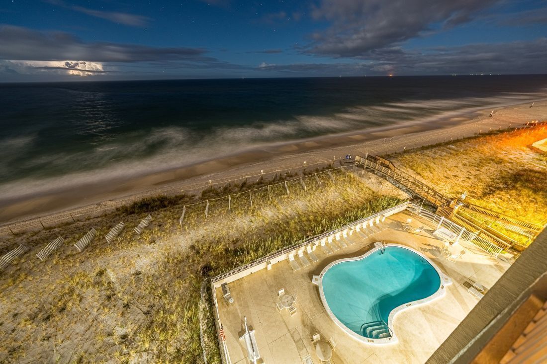 A pool area with a view of the beach and ocean at night.