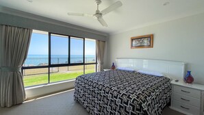 A bedroom with a large bed, a ceiling fan, a window with a view of the beach, and a framed picture on the wall. - Seahaven - Located in Toogoom (TOOGOOM)