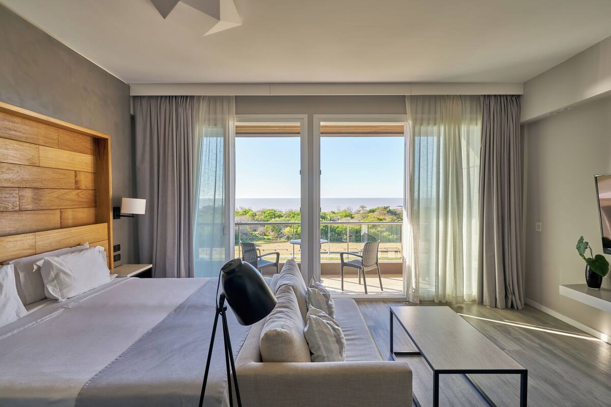 Een moderne hotelkamer met een groot bed, een slaapbank, een bureau en een balkon met uitzicht op zee.