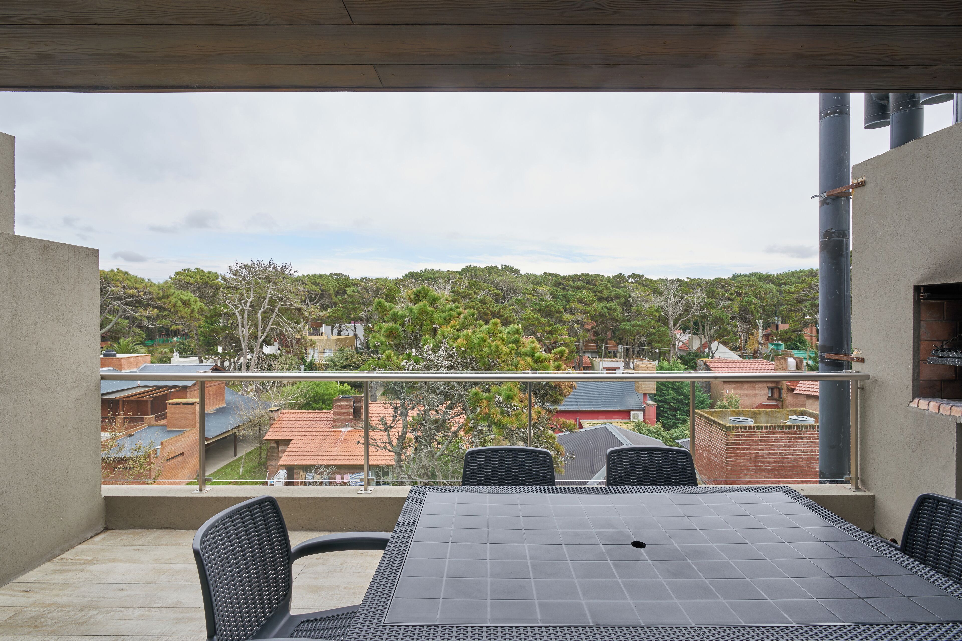 A balcony with a table and chairs, overlooking a residential area with trees and houses.