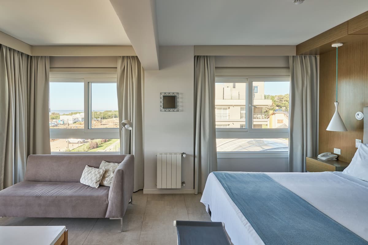 Een hotelkamer met een bed, een bank, uitzicht op de stad en een raam met gordijnen.