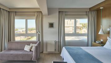 Habitación de hotel con cama, sofá, vista de la ciudad y ventana con cortinas.