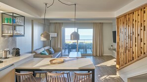 Een moderne woonkamer met een groot raam, een bank, een eethoek met een tafel en stoelen, en een keuken met een koffieapparaat en planken.