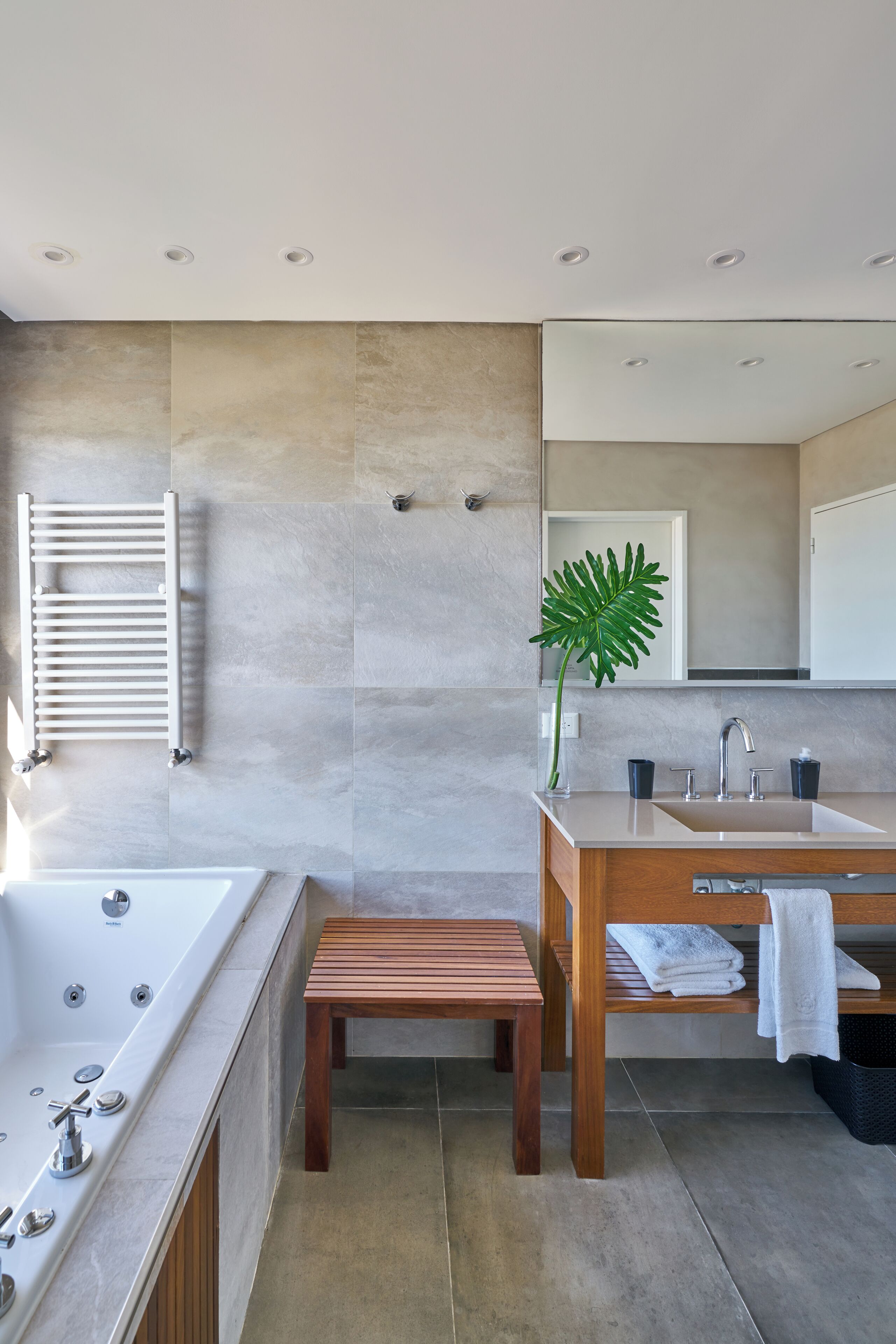 A modern bathroom with a large bathtub, wooden bench, two sinks, and a mirror.