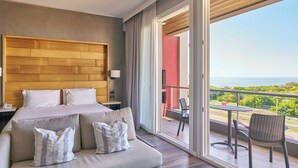 Een moderne hotelkamer met een groot bed, een balkon met uitzicht op zee en een zithoek met een tafel en stoelen.