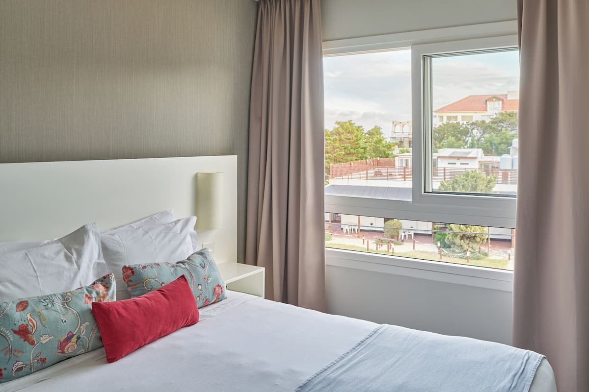 Een hotelkamer met een groot bed, een hoofdeinde, een raam met gordijnen en een plafondlamp.