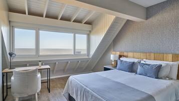Un dormitorio con una cama grande, un escritorio y una silla. Se ve el cielo a través de la ventana.
