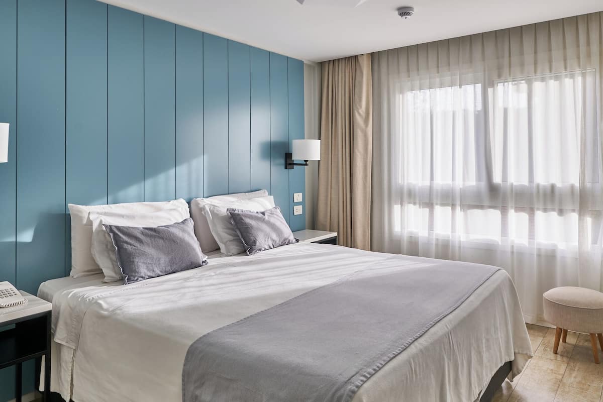 Een moderne hotelkamer met een groot bed, nachtkastje, lamp en een raam met gordijnen.