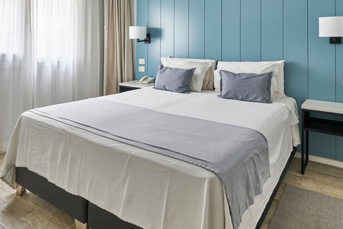 Een moderne hotelkamer met een groot bed, twee nachtkastjes, een wandlamp en een plafondlamp.