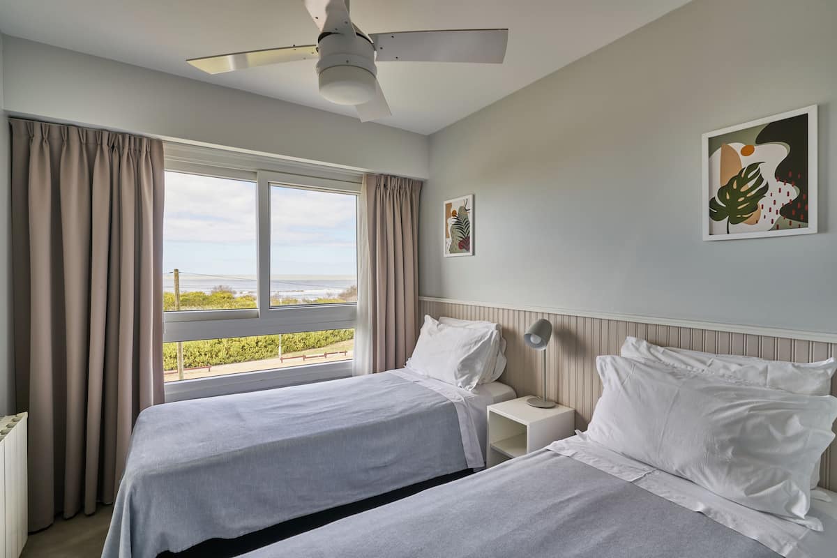 Een hotelkamer met twee bedden, een plafondventilator, een raam met gordijnen en kunst aan de muur.