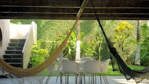 A covered outdoor seating area with a table and chairs, a hammock, and a staircase leading to an upper level.