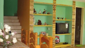 A dining area with a wooden table and chairs, a television on a shelf, and a staircase leading to another room. - L'AMARELA MANSION 11 SUITES 50 BEDS NEIGHBORHOOD TO BEACH PARK (AQUIRAZ)