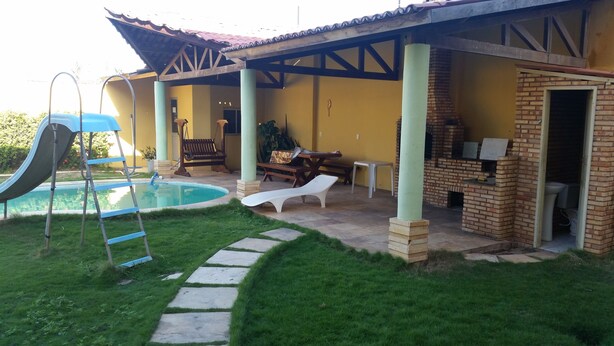 A backyard with a swimming pool, a slide, lounge chairs, a barbecue area, and a patio with a table and chairs. - L'AMARELA MANSION 11 SUITES 50 BEDS NEIGHBORHOOD TO BEACH PARK (AQUIRAZ)
