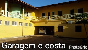 A yellow building with a covered parking area and a white van parked inside. - L'AMARELA MANSION 11 SUITES 50 BEDS NEIGHBORHOOD TO BEACH PARK (AQUIRAZ)