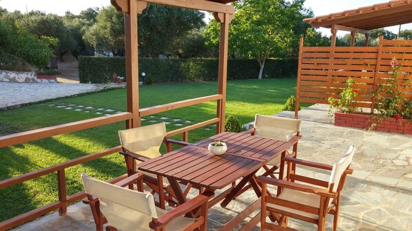 Une pergola en bois avec une table et des chaises, entourée d’un jardin bien entretenu et d’un sol pavé de pierres.