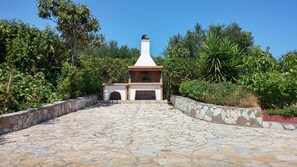 A stone pathway leading to a white and brown outdoor grill area surrounded by lush greenery.