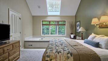 Un dormitorio con una cama grande, televisión, ventana con vistas a árboles, tragaluz y bañera.