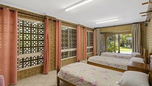 Habitación de hotel con dos camas, una pared de ladrillo y ventanas amplias con cortinas.