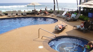 Un espace piscine doté de chaises longues et de parasols, avec vue sur l’océan.