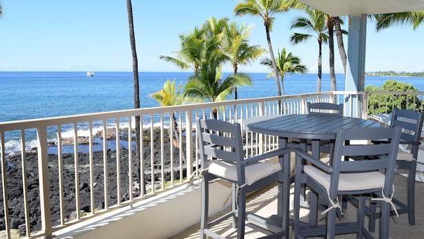 Un balcon avec une table et des chaises donnant sur une côte rocheuse et l’océan.