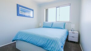 A bedroom with a bed, a nightstand, a window, and a framed picture on the wall. - Explorer Cove Unit 6, 31 Kennedy Pde (GOLDEN BEACH)