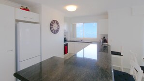 A modern kitchen with white cabinets, a black granite countertop, a built-in oven, and a window providing natural light. - Explorer Cove Unit 6, 31 Kennedy Pde (GOLDEN BEACH)