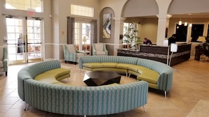 Eine Lobby mit einem gebogenen, grünen Sofa, einem Empfangstresen und einem großen Fenster.