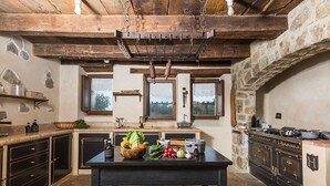 Une cuisine rustique avec un mur en pierre, des poutres en bois et une table noire sur laquelle sont disposés des légumes frais.