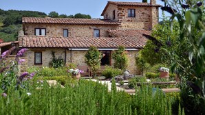 Une maison en pierre avec un toit en tuiles, entourée d’un jardin bien entretenu où poussent différentes plantes et fleurs.